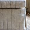 Side detail of ottoman showing cushioned top and skirt with vertical stripes resting on patterned area rug