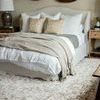 Different styling angle of Blake duvet with beige and white decorative pillows and textured throw on bed with woven wall d...