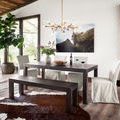 Cowhide rug under dark wood dining table and bench in bright room with large windows and modern chandelier