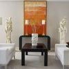 Console table placed in living room setting between white sofas with abstract orange artwork on wall