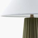 Detail of white linen fabric lamp shade and brass socket atop olive green ribbed base