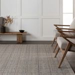 Rug placed on wood floor next to wooden chairs and minimalist bench against white paneled wall