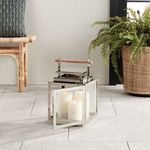 Outdoor lantern with open door revealing white pillar candles inside on patio floor