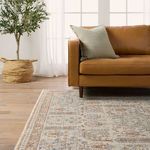 Side view showing rug extending under caramel leather sofa with green pillow and natural light