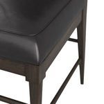 Close-up of black leather seat upholstery with detailed stitching and ebony wood frame corner