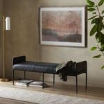 Side view of framed landscape painting hanging in warm-toned minimalist room with black bench