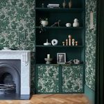 Living room corner styled with Enzia Emerald wallpaper, green shelves, marble fireplace, and wooden herringbone floor