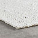Side angle showing the rug's low profile edge resting on gray hardwood floor