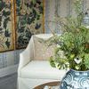 Close-up of vase with floral arrangement showing cream-colored armchair and decorative wall panels