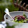 Side view of white stoneware bowl filled with mixed greens salad and two silver serving forks