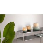 Same three greenish glass lantern vases on metal shelf with candles lit inside providing warm glow