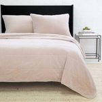 Twin-sized Amsterdam Coverlet in soft blush with a quilted square pattern layered on a bed with matching pillow shams