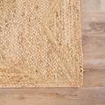 Close-up of braided border detail with varied weave texture on beige natural fiber rug
