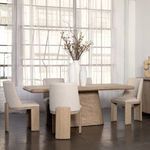 Marci dining table styled in a bright room with six beige upholstered chairs and tall decorative vases on top