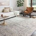 Lucia Grey / Mist rug shown in a living room with white sofa, leather chair, and natural light from window