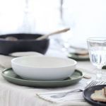Artichoke plate holding a white matte bowl, styled on a linen table with glassware and silverware
