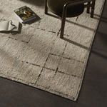 Rug styled in a room setting under a chair with books and natural sunlight emphasizing textile texture