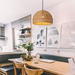 Woven pendant light hanging above dining table in modern room setting with artwork and chairs