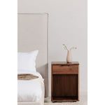 Osamu nightstand styled next to a beige upholstered bed with a small vase on top