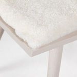 Close-up on off-white sheared sheepskin cushion with plush texture atop wooden seat