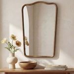 Keyes mirror mounted above wooden console with cream vase and wooden bowl in warm light room setting