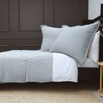 Light gray Monaco coverlet and matching pillows with diamond quilted pattern and 1-inch flange on bed in neutral room