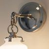 Close-up view of metal arm and polished round backplate with frosted glass shade lit softly