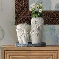 Three white floral vases displayed on wooden console table with greenery inside tallest vase and textured wall art behind