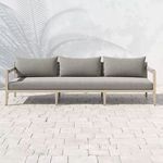 Front view of sofa outdoors on stone patio with palm leaf shadow on white stucco wall