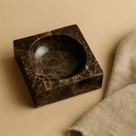 Square marble bowl shown in warm beige room setting with textured fabric nearby