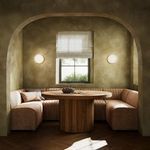 U-shaped dining banquette set around a round wood table in a sunlit arched nook with window and sconces