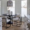 Two Sanya Metal Vases on dining table with black base surrounded by white upholstered chairs in a bright room with large w...