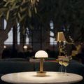 Promenade lamp lit on round table in dim room with dark green sofa and glasses of white wine