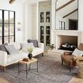 Multi rug styled in a bright living room under a white sofa and brown armchair with wooden beams and mirror above fireplace