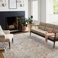 Styled living room setting with Rosemarie rug beneath mid-century modern sofa and chairs by a stone fireplace