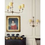 Wall sconce lit in a traditional styled room with framed portrait and additional chandelier overhead