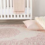 Rug partially under crib with folded pink throw and pillows on soft beige wood floor
