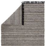Rug corner folded over showing striped underside in black and gray with black fringe.