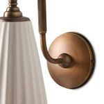 Close-up of round brass wall plate with screw details and attached curved arm of Wilma Sconce