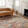 Jocelyn Mist / Multi Rug layered in a living room with a tan leather sofa, white fireplace, and woodside table