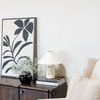 angled view of painting on wood cabinet beside white lamp and beige upholstered chair in neutral room