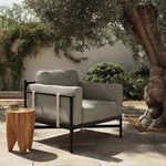 Hearst Outdoor Chair shown outdoors beside large tree and wooden side table with glass