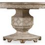Round wooden dining table with scallop motif fretwork on apron and pedestal base, distressed light finish