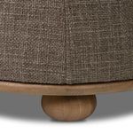 Detailed view of lower ottoman side seam above sandy oak base and round wooden bun foot