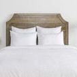 Front-facing view of white duvet and pillows styled on bed with wooden headboard and bedside accessories