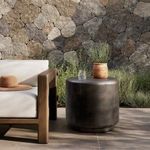 Outdoor end table styled next to wooden-framed couch with hat, glass, and planter on top