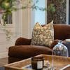 Pillow cover on armchair with woven tray and decorative items in foreground, cozy interior context