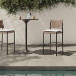 Outdoor setting with stool by round pedestal table beside pool and white wall background