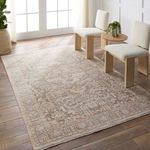 Rug displayed in a bright room setting with two cream-colored chairs and a small round wooden table