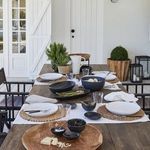 Outdoor dining table set with multiple matte black ceramic dishes including oval platter, styled with food and drink
